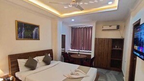 Una habitación de hotel con cama, mesita de noche, televisión y un pequeño comedor.