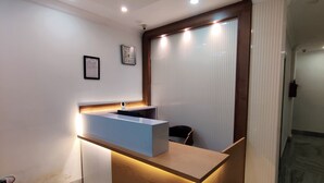 Un mostrador de recepción con encimera de madera y un panel azul, un reloj en la pared y una silla al frente.