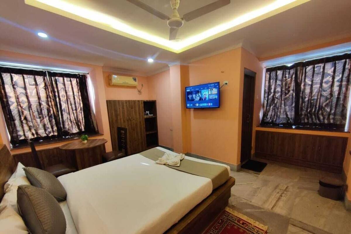 A hotel room with a bed, a television mounted on the wall, and a window with curtains.