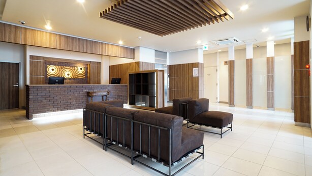 A modern reception area with a brick wall, wooden paneling, and a seating area with sofas and a bench. - Hotel BRS Hakodate Goryokaku Tower (Hakodate)