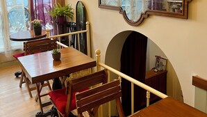 A dining area with wooden tables and chairs, a large mirror, and a view of the outdoors through sheer curtains. - Levant Pension de Luxe  (Istanbul)