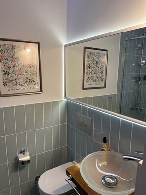 A bathroom with a toilet, a sink with a wooden countertop, a mirror, and two framed floral artworks on the wall.