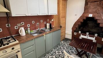 Una cocina con estufa a gas, lavamanos y armarios de madera. Hay un horno de ladrillo y una silla en la esquina.