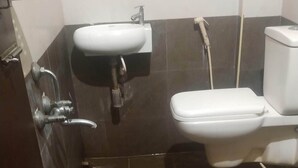 A bathroom with a sink, toilet, and a large plastic container on the floor. - Hotel RAAJASGRAND (Tirupati)