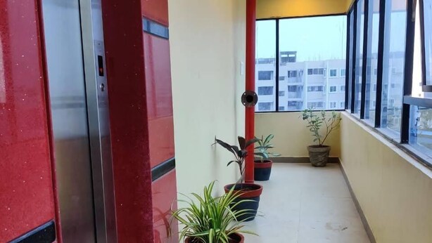 A corridor with potted plants, a red pillar, and a view of buildings through large windows. - Hotel RAAJASGRAND (Tirupati)