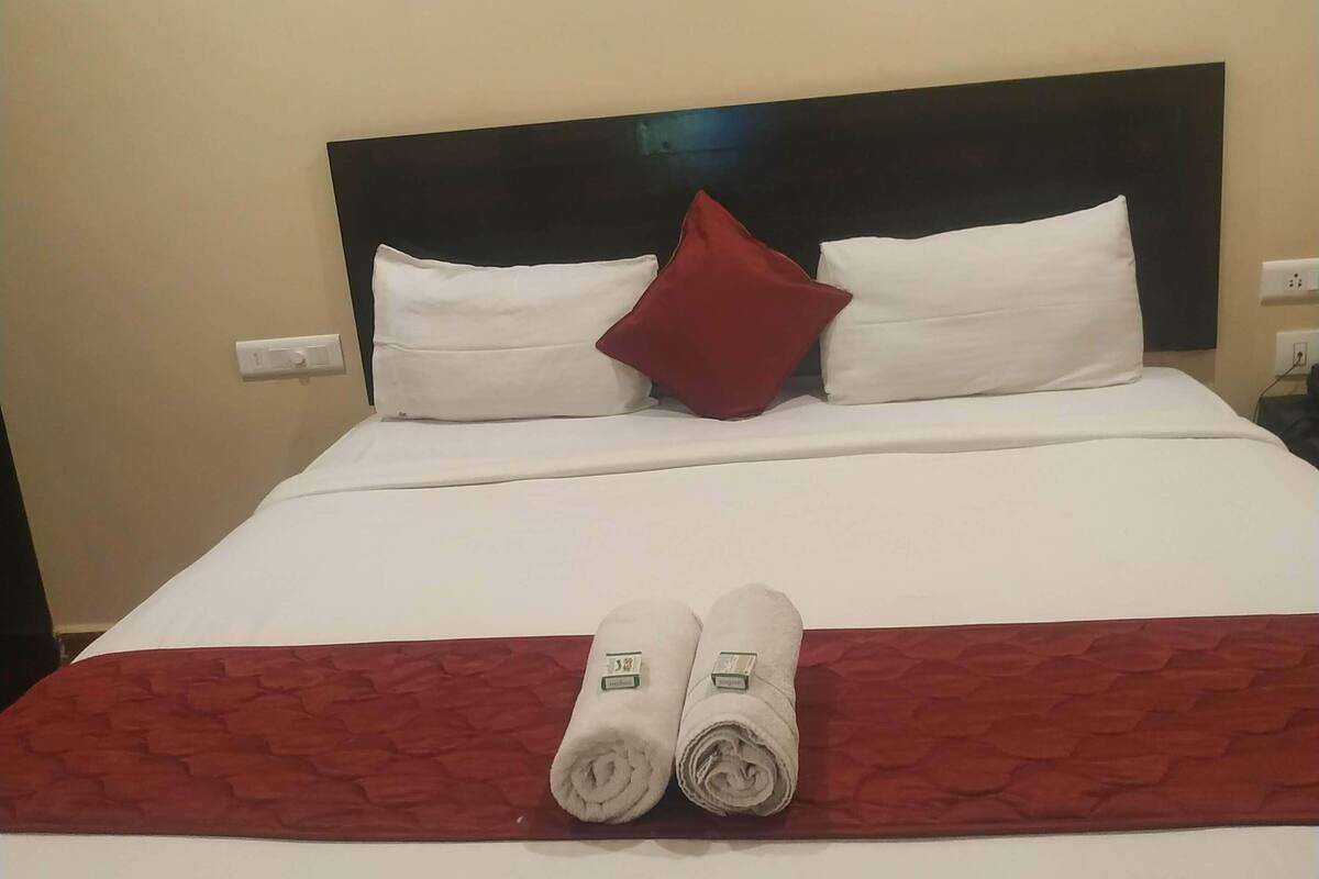 A neatly made bed with white linens, a red throw, and two rolled towels.