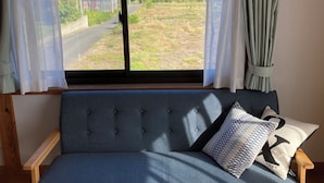 Ein Zimmer mit einem blauen Sofa, Holzboden und einem Fenster mit Vorhängen.