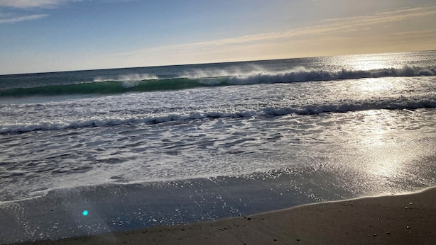 Ein Strand mit Wellen und Sonnenlicht, das sich im Wasser spiegelt.