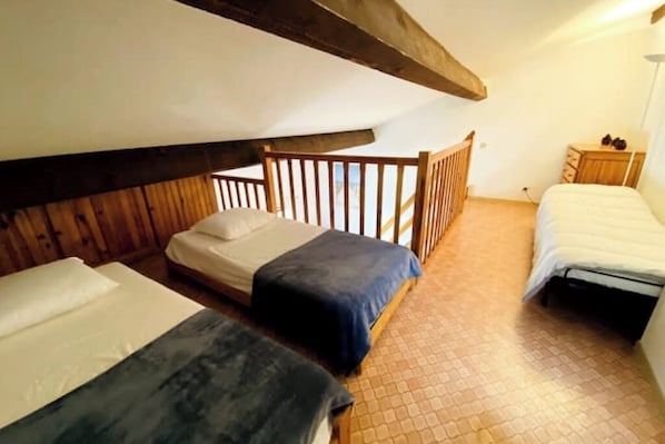 A small, cozy room with two beds, wooden beams, a wooden railing, and a small wooden dresser.