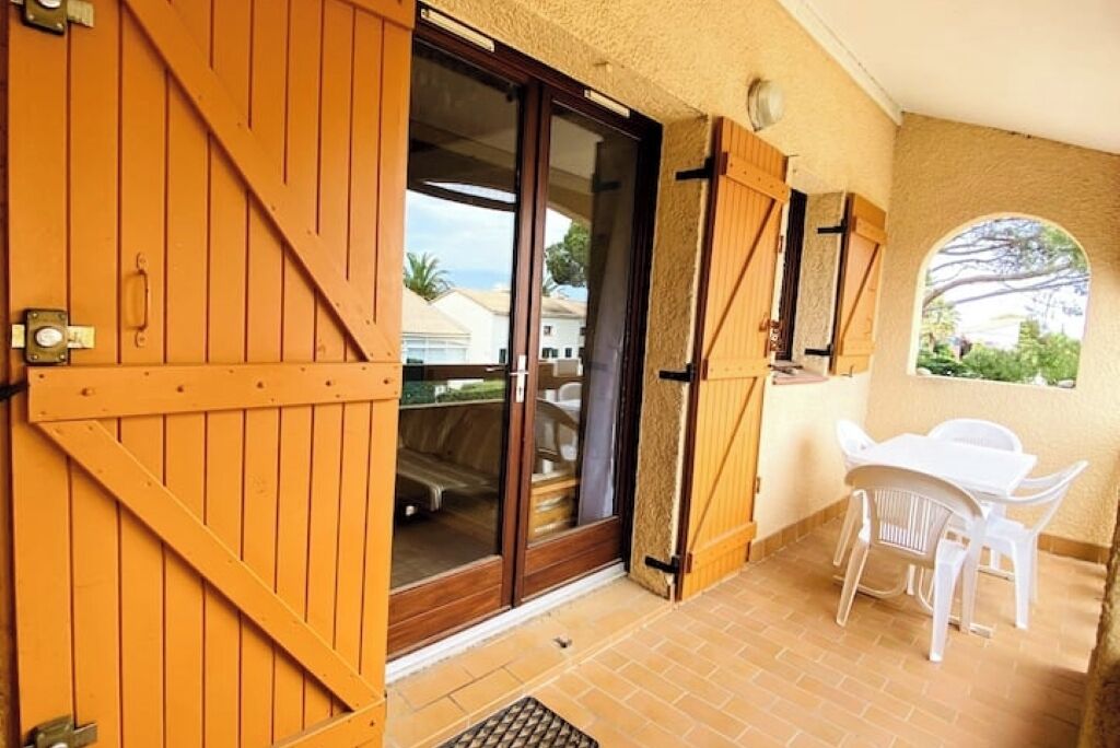 Un espace extérieur abrité, doté d’une porte-fenêtre coulissante donnant sur une terrasse avec une table et des chaises blanches.