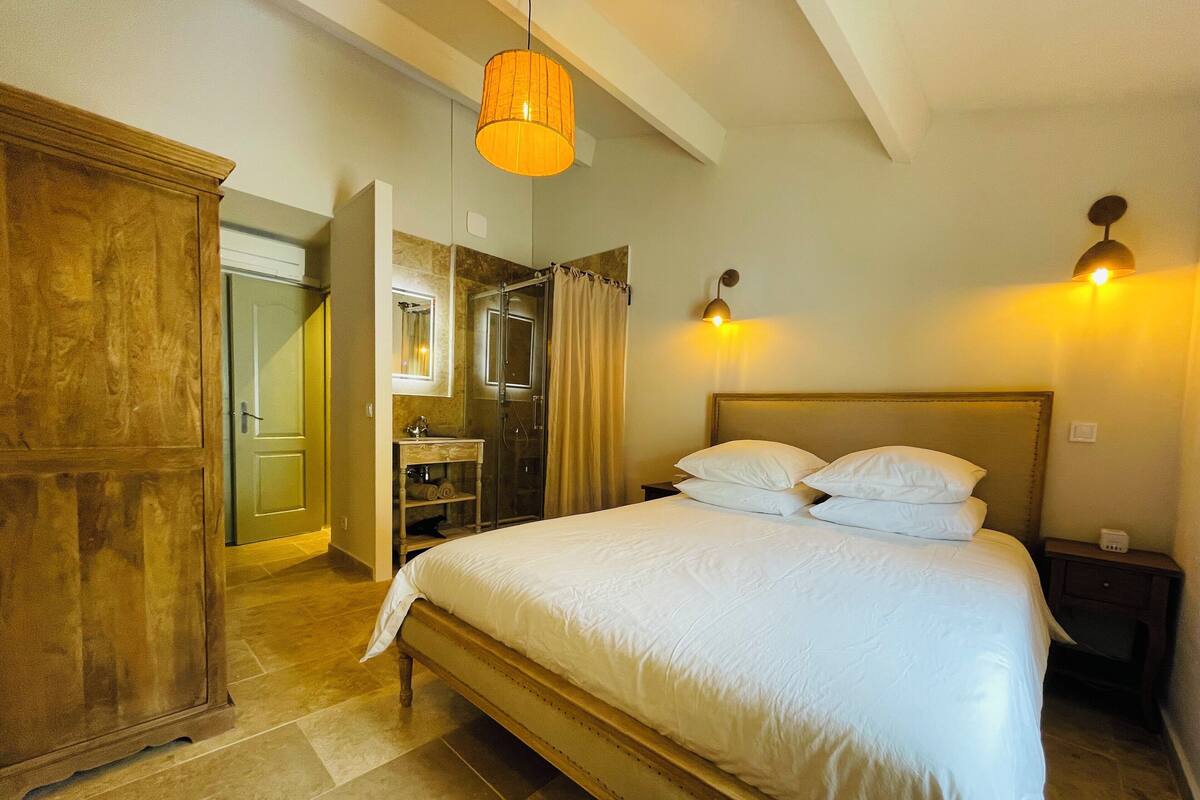 Un dormitorio con una cama grande, armario de madera y baño con ducha y tocador.
