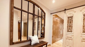 A hallway with a wooden bench, a large mirror, and a door with decorative metal bars. - La Réserve Provence (Vaugines)