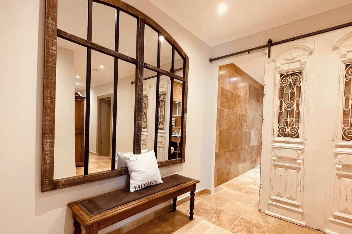 Un pasillo con un banco de madera, un espejo grande y una puerta con barandales decorativos.