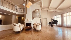 A spacious living room with a fireplace, a grand piano, and a high ceiling with exposed beams. - La Réserve Provence (Vaugines)