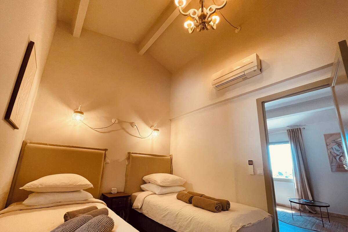 Habitación de hotel con dos camas, una araña y aire acondicionado, con vista al exterior.