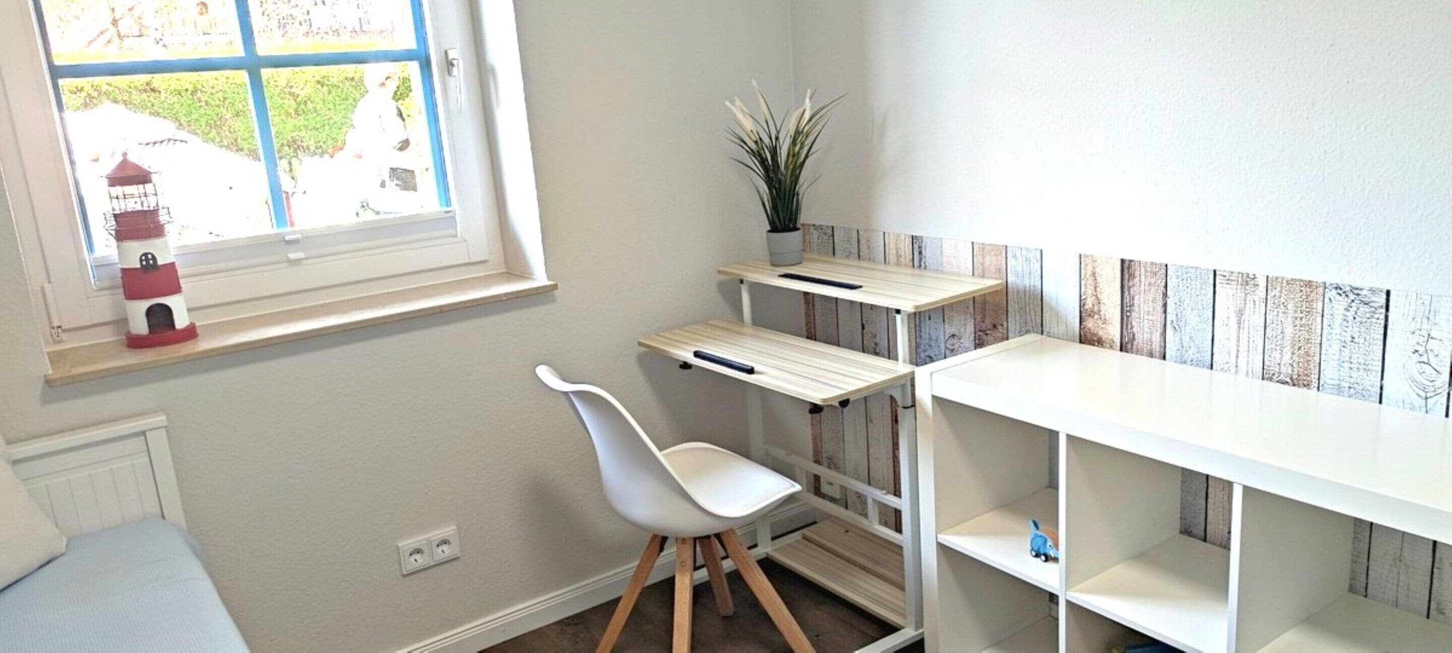 A child's room with a white chair, a small table, a shelf with a plant, and a window with a view of greenery.