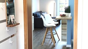 Ein modernes Wohnzimmer mit einem dunklen Sofa, weißen Stühlen, einem kleinen Tisch und einem Fenster mit Jalousien.