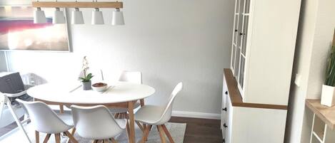 A modern dining area with a round table, white chairs, and a potted plant.