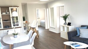 Ein modernes Wohnzimmer mit einem grauen Sofa, einem Esstisch mit Stühlen und einer Küchenzeile mit Schränken und einer Pendelleuchte.