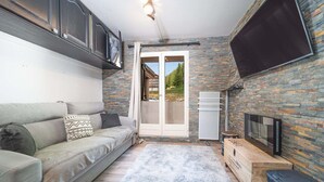 A compact living space with a sofa, a TV mounted on the wall, and a sliding glass door leading to an outdoor area.
