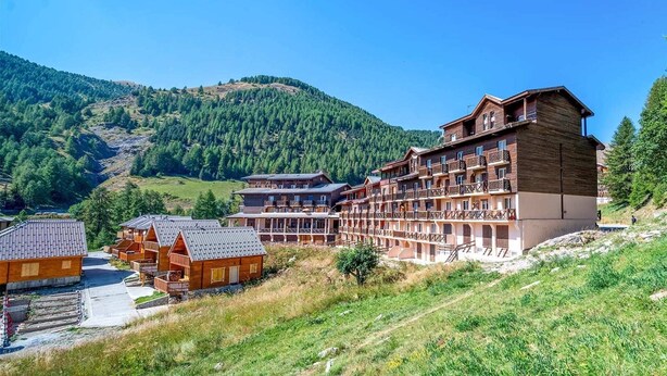 A hotel with multiple wooden buildings, balconies, and a mountainous backdrop.