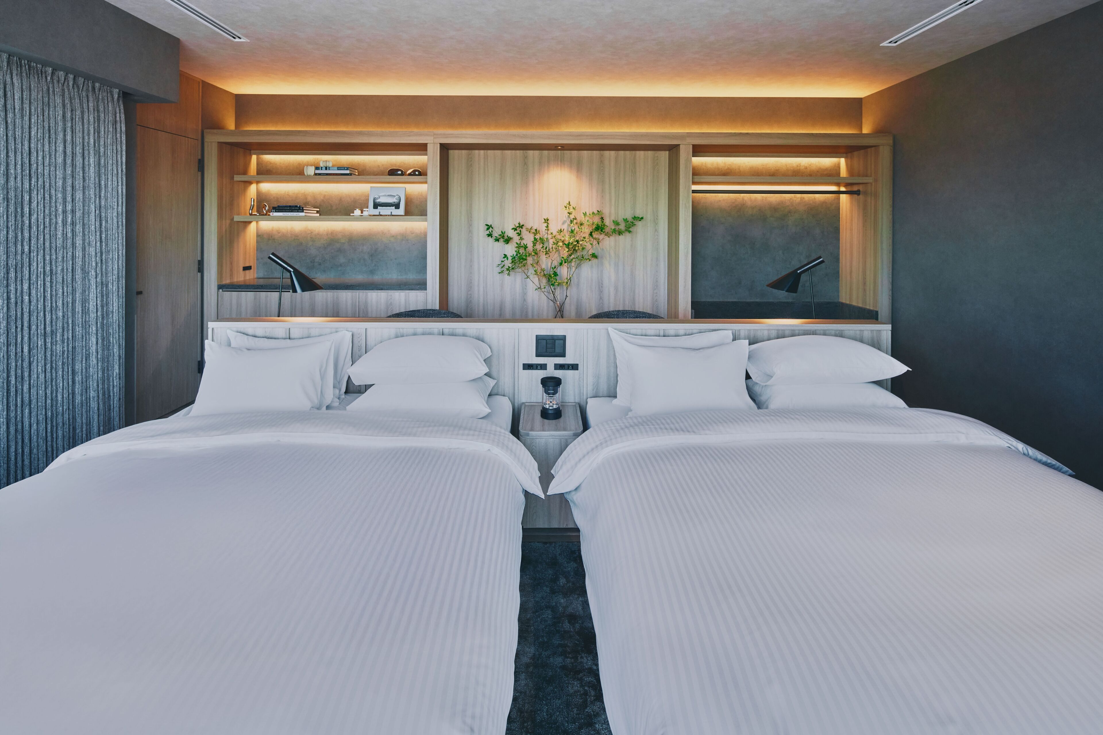 A double bed room with a bedside table, a small bedside lamp, and a wall-mounted shelf with a plant.
