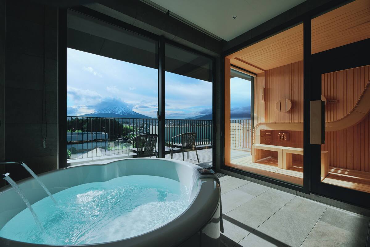 Ein moderner Wellnessbereich mit Whirlpool, Holzsauna und einem Balkon mit Bergblick.