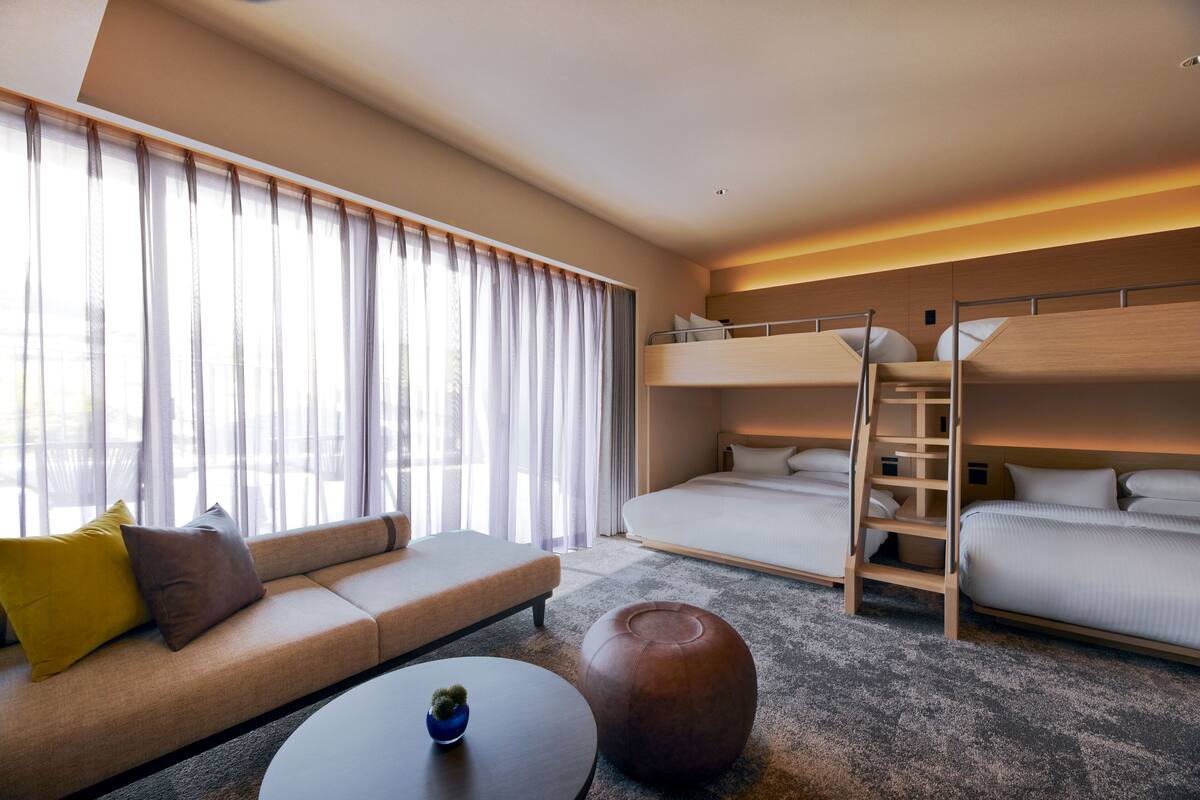 Ein Hotelzimmer mit einer Couch, einem Bett, einem Stockbett, einem Couchtisch und einem großen Fenster mit Vorhängen.
