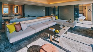 Un salon moderne doté d’un grand canapé d’angle, d’une table basse et d’un coin salon agrémenté d’un petit pouf.