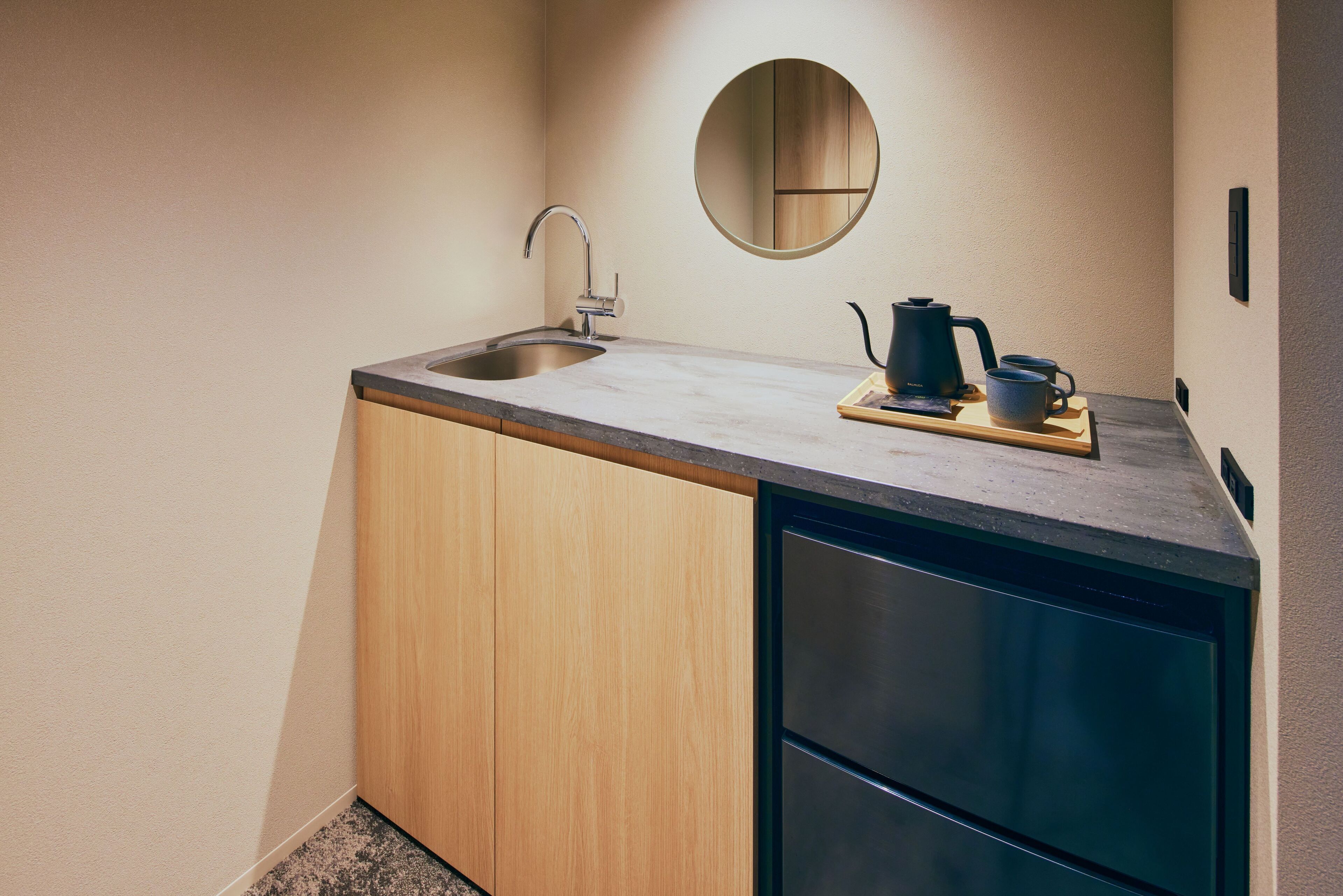 A compact kitchen with a sink, a coffee maker, and a small mirror on the wall.