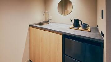 A compact kitchen with a sink, a coffee maker, and a small mirror on the wall.