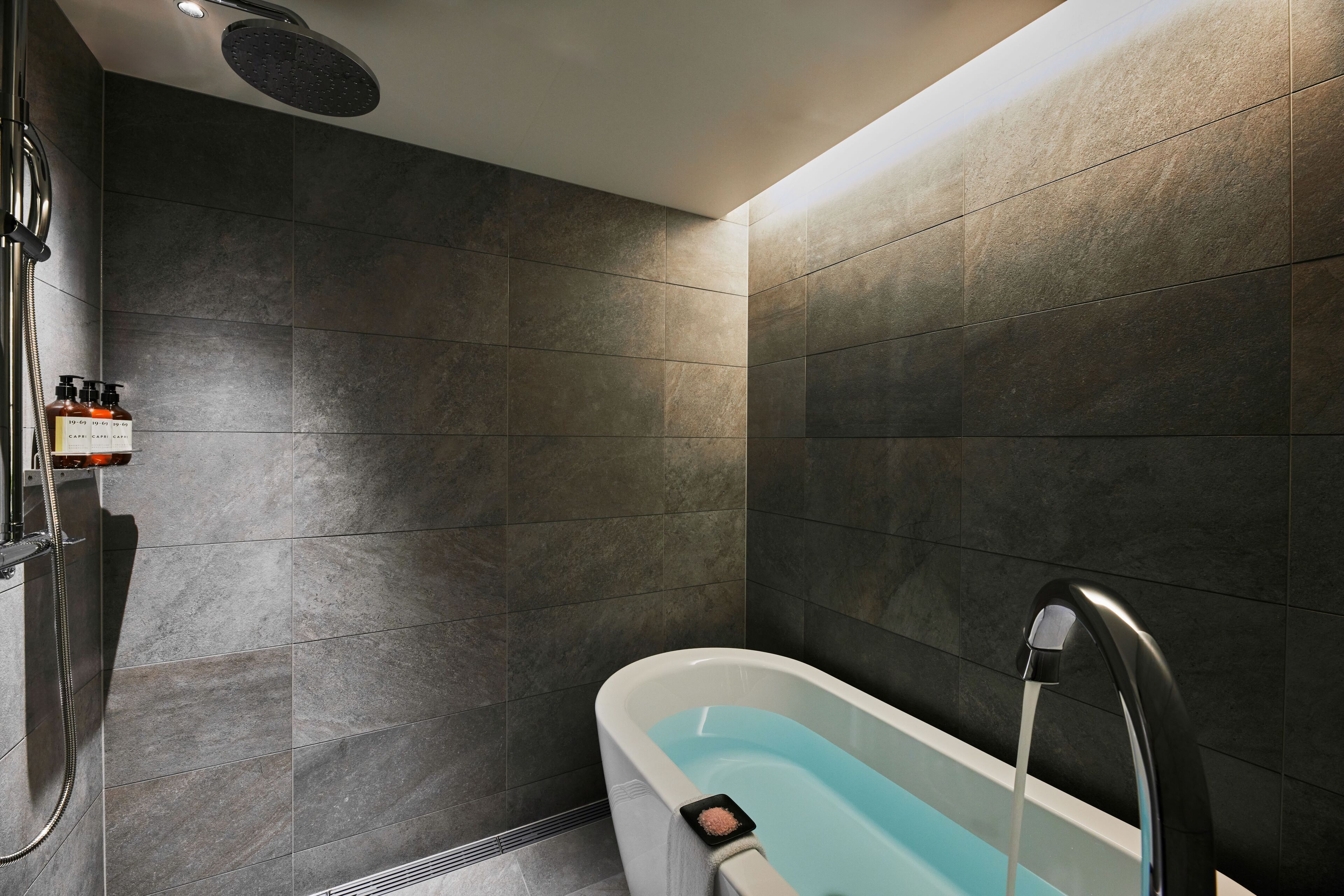 A modern bathroom with a bathtub, shower, and a bottle of shampoo on the wall.
