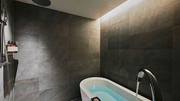 A modern bathroom with a bathtub, shower, and a bottle of shampoo on the wall.