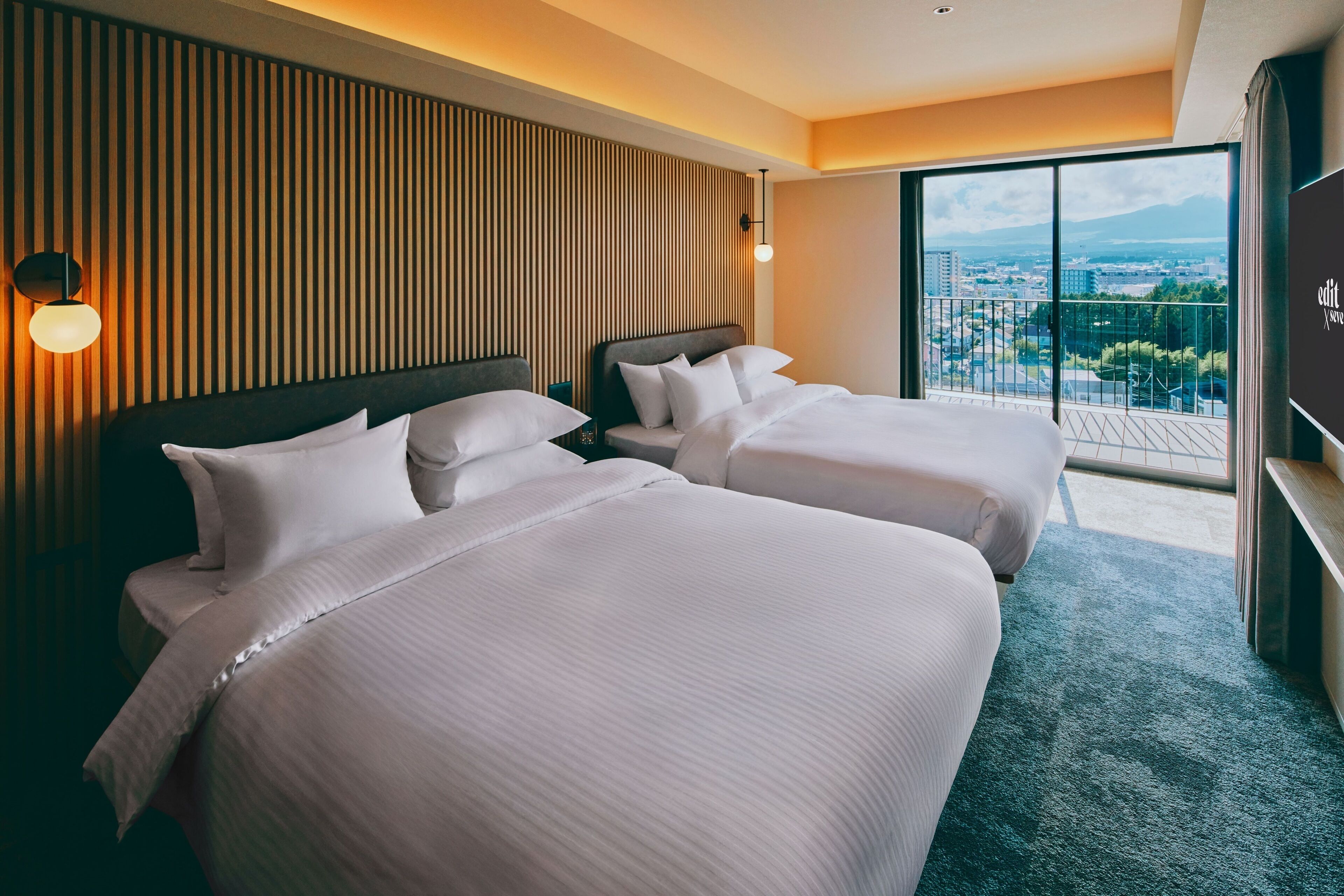 A hotel room with two beds, a large window with a city view, and a wooden panel wall.