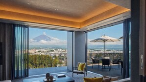 Une chambre d’hôtel moderne dotée d’un grand balcon, d’un canapé, d’une table basse et offrant une vue sur le paysage urbain et un volcan.