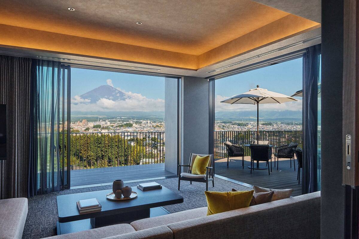 Ein modernes Hotelzimmer mit großem Balkon, einer Couch, einem Couchtisch und Blick auf Stadt und Vulkan.