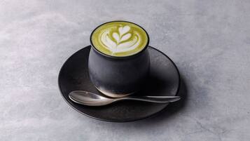 A cup of green tea latte with latte art on a black saucer and spoon.