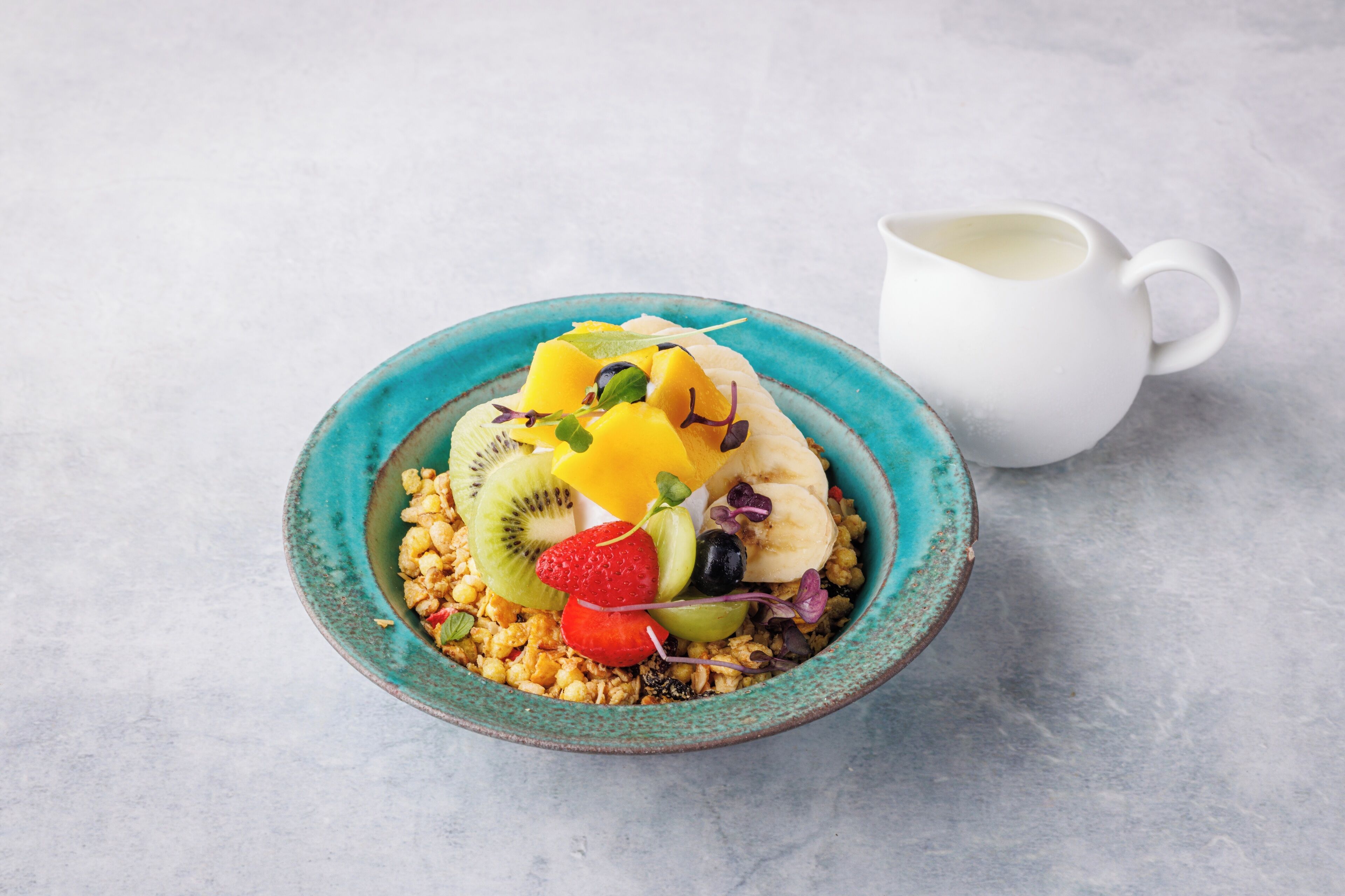 Un tazón de cereal con frutas y una jarrón blanco sobre una mesa.