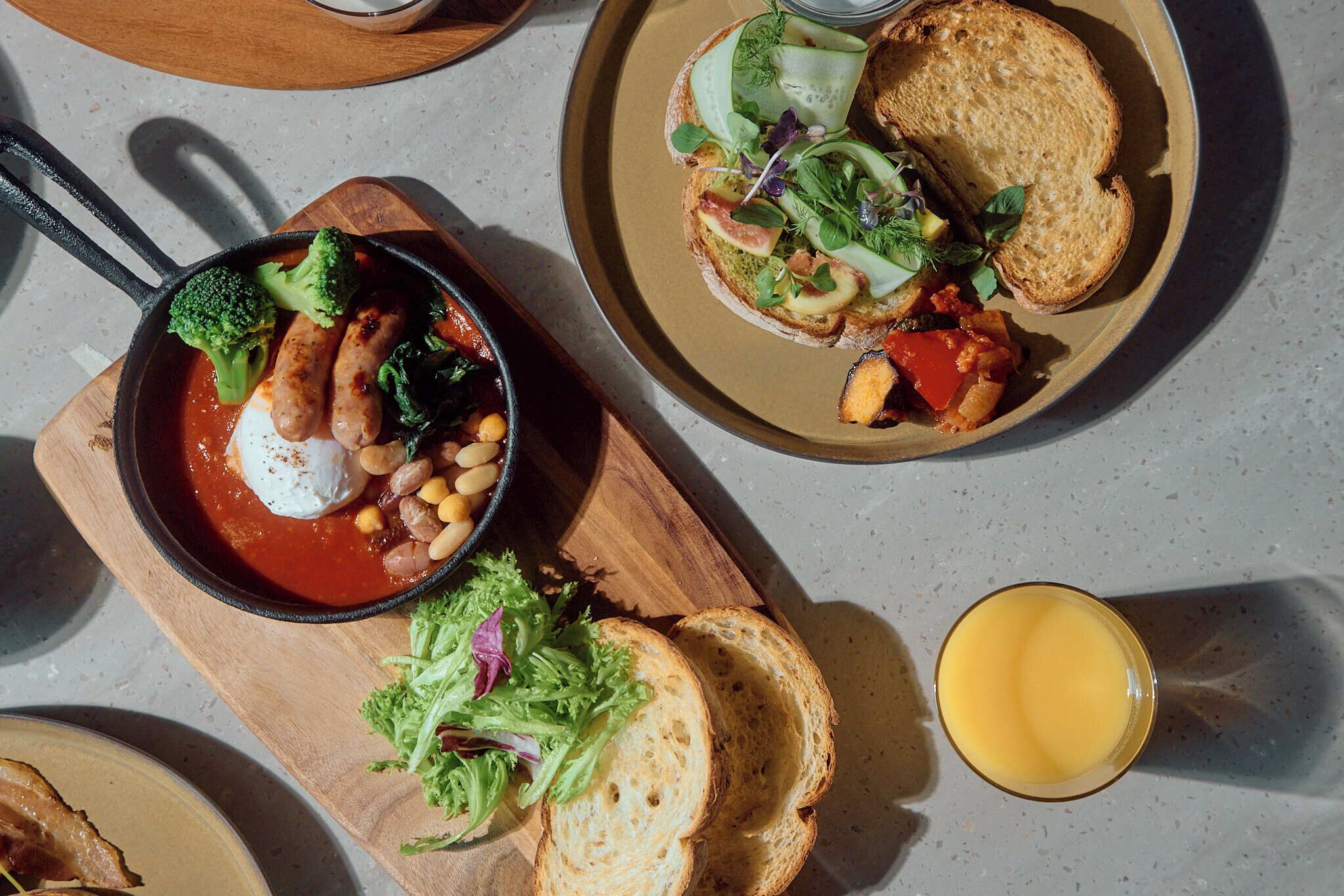 A meal with a variety of dishes including a skillet with vegetables and beans, a plate with bread and salad, and a glass of juice.