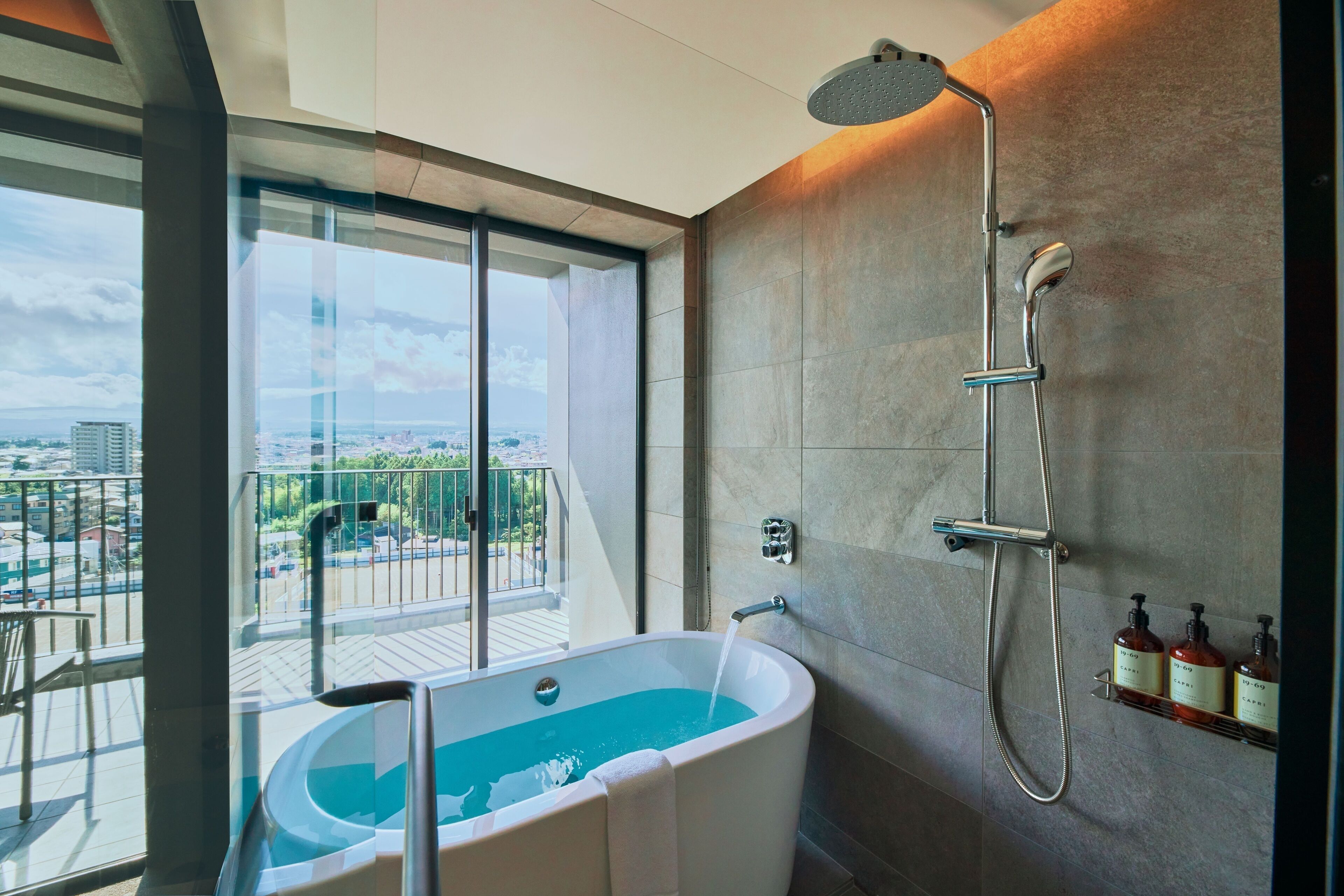 A modern bathroom with a freestanding bathtub, a showerhead, and a view of the city through large windows.