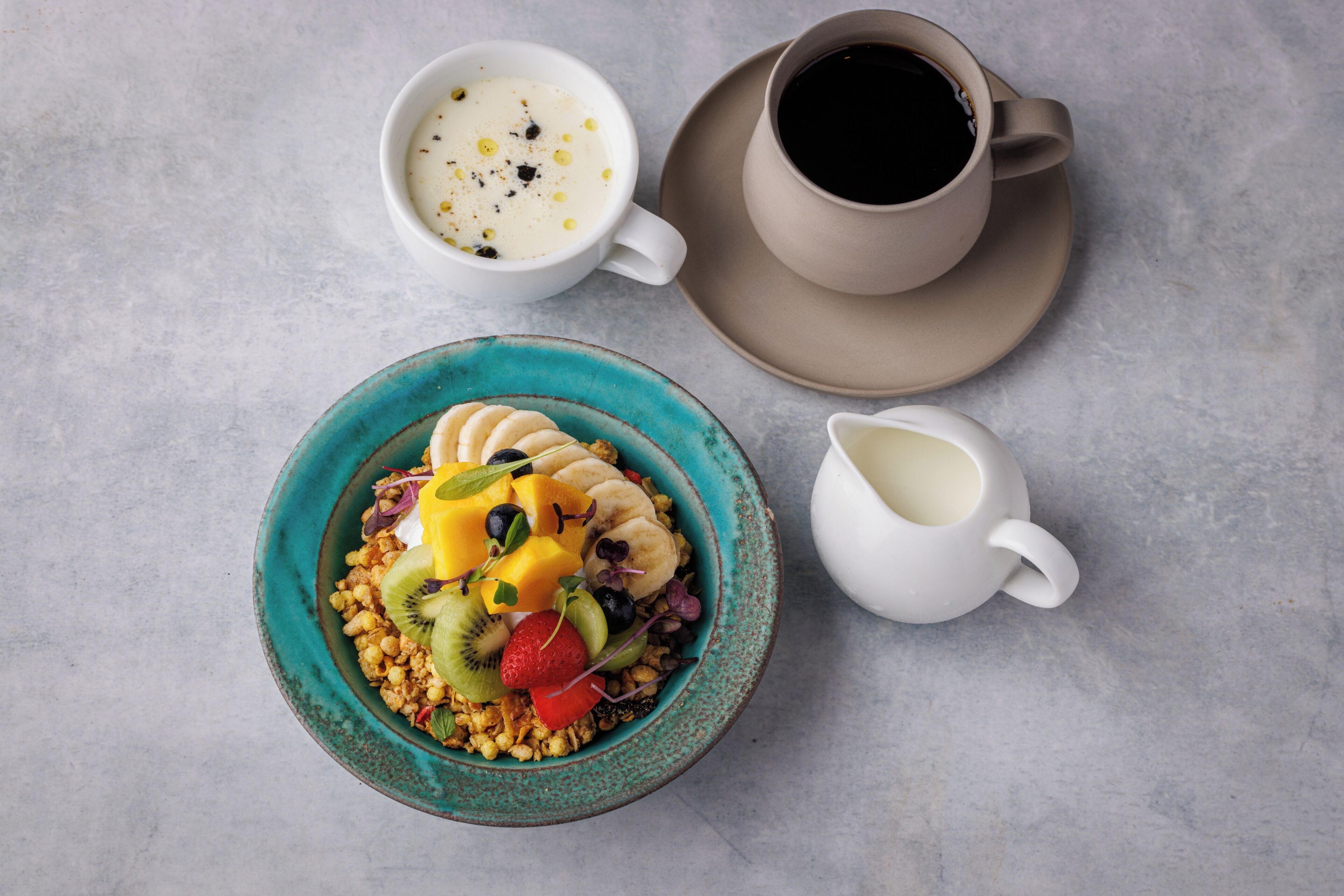 A breakfast setting with a bowl of cereal topped with fruits and a cup of coffee.