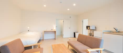 A modern, well-lit room with a bed, two sofas, a small table, and a kitchenette.