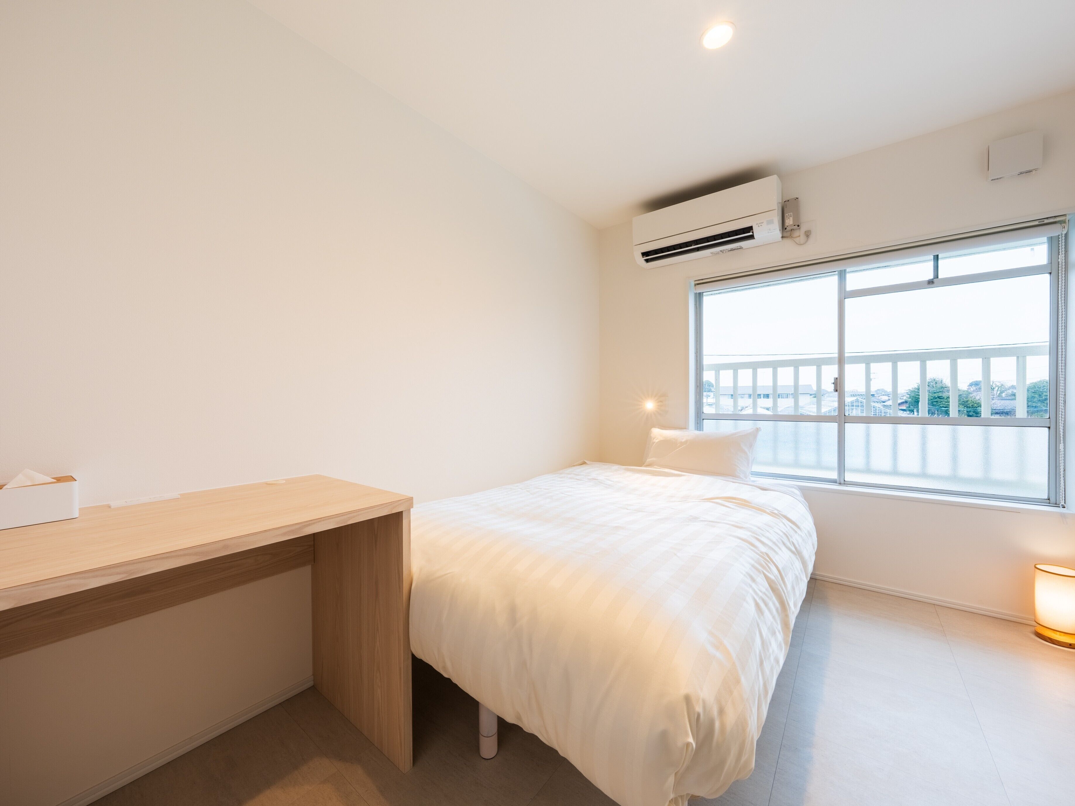 A minimalist bedroom with a bed, a bedside table, a window with a view, and an air conditioning unit.