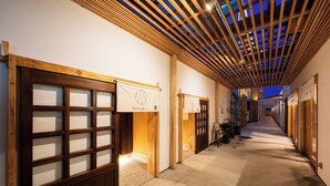 A corridor with wooden paneling and glass doors, leading to a reception area with a sign. - HOTEL MEGURI (Usa)