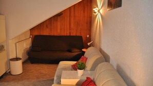 Un salón acogedor con un sofá marrón oscuro, un sofá gris claro, una mesita blanca con una planta y una lámpara fijada a la pared.