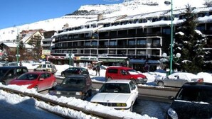 Un hotel de varios pisos, un estacionamiento con coches y una montaña nevada al fondo.