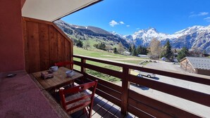 A balcony with a wooden table and chairs, overlooking a mountain landscape with a clear sky. - Ski-In Stay in Les Deux Alpes (Les Deux Alpes)