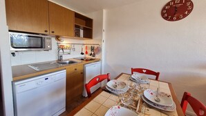 A compact kitchen with a microwave, dishwasher, and a dining table set for two with red chairs. - Ski-In Stay in Les Deux Alpes (Les Deux Alpes)