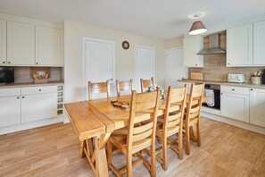 A compact kitchen with white cabinets, a wooden dining table, and a built-in oven. - Host Stay Audrey s Cottage (Kelso)