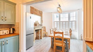 A kitchen with light blue cabinets, a brick wall, a stainless steel refrigerator, and a dining area with wooden chairs and a table. - Host Stay Bedford Street (Brighton)